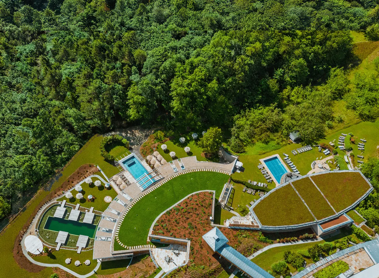 Luftaufnahme des RETTER Bio-Natur-Resorts mit grünen Dächern, Naturbadeteich und Pools inmitten üppiger Wälder.