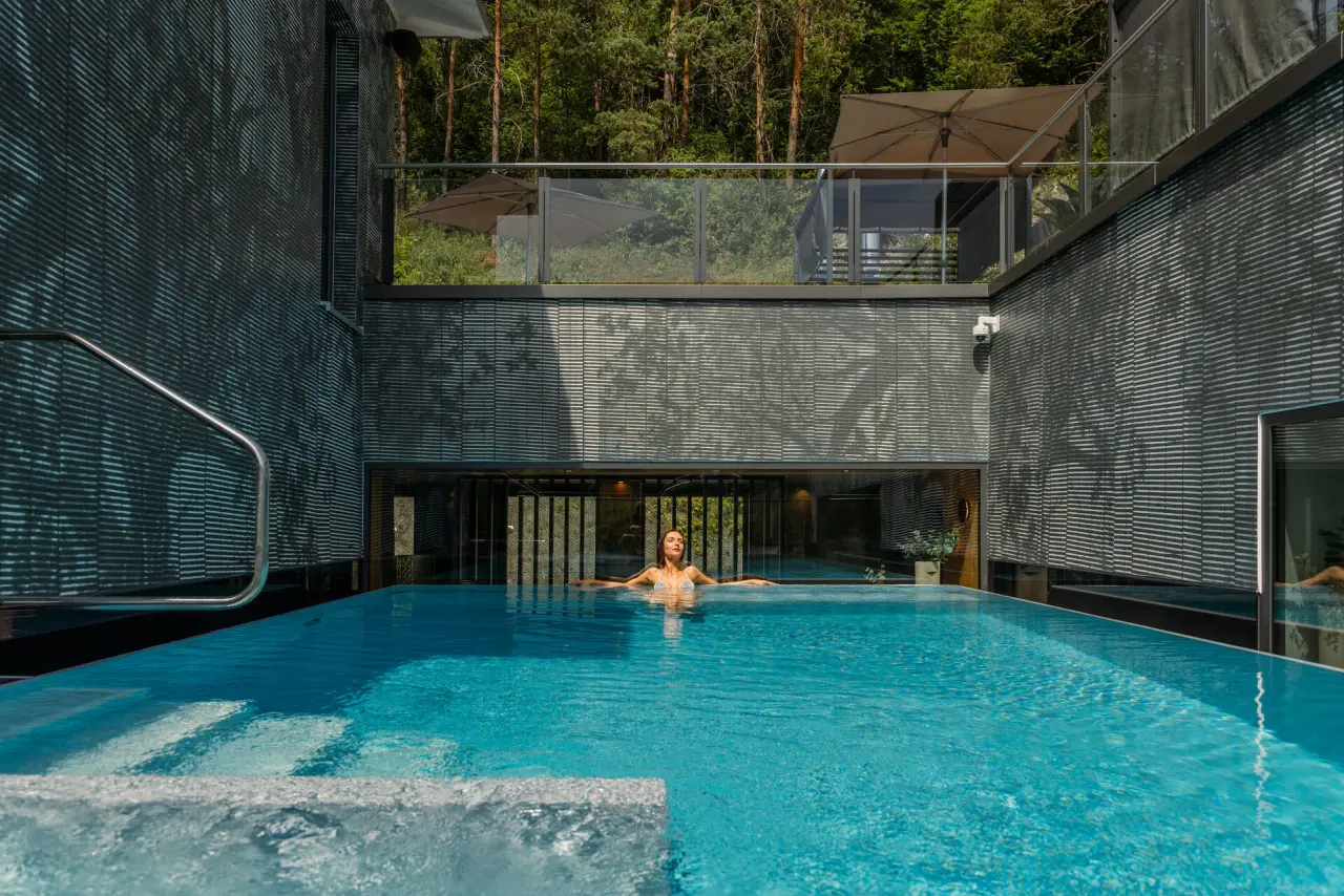 Modernes Indoor-Outdoor-Pool im Wellnesshotel Sternwirt mit Blick auf den Wald und entspannter Badegästin.