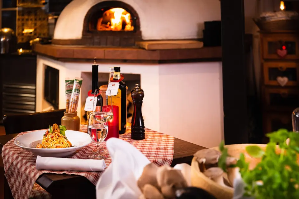 Gemütliches Restaurant im Hotel BEI SCHUMANN mit Holzofen, gedecktem Tisch, Pasta, Wein und mediterranem Flair.