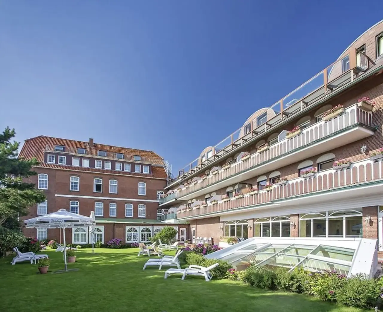 Aussenansicht des Nordseehotel Freese mit gepflegtem Garten, Liegestühlen und blühenden Balkonen unter blauem Himmel.
