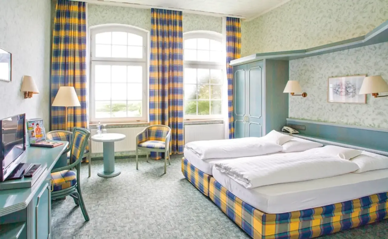 Gemütliches Doppelzimmer im Nordseehotel Freese mit karierten Vorhängen, zwei Einzelbetten und Schreibtisch.