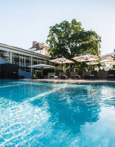 Sonniger Aussenpool mit blauer Wasseroberfläche, Liegestühlen und Sonnenschirmen im Steigenberger Sonnenhof Hotel.