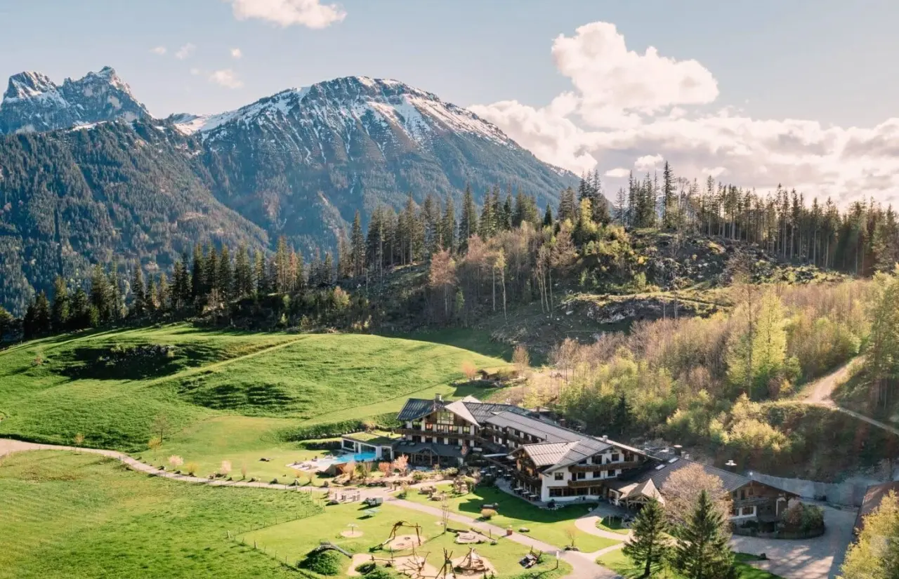 Schlossanger Alp Hotel in den Allgäuer Alpen mit Aussenpool, umgeben von grünen Wiesen und schneebedeckten Bergen.