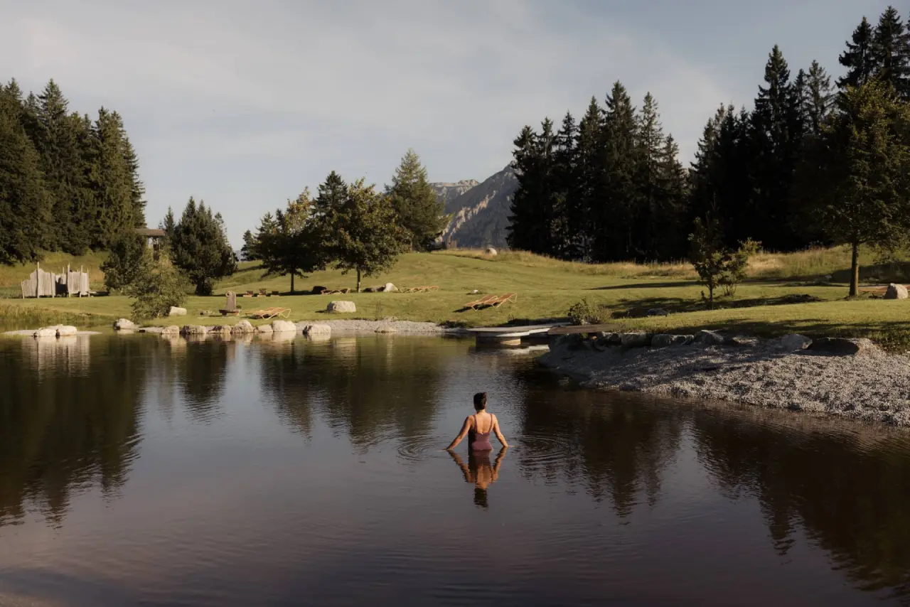 Naturbadeteich mit Schwimmerin und Alpenpanorama im Garten des Schlossanger Alp Hotels