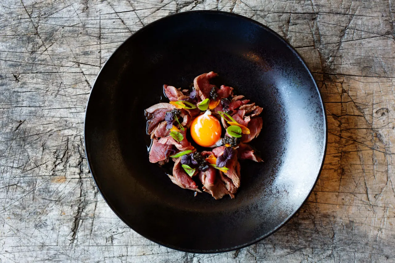 Exquisites Gourmetgericht mit Rindfleisch, Eigelb und Kaviar auf schwarzem Teller im Restaurant der Schlossanger Alp.