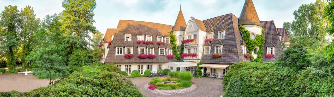 Idyllische Aussenansicht des Landhaus Wachtelhof mit charmantem Fachwerk, blühenden Blumenkästen und üppigem Grün.