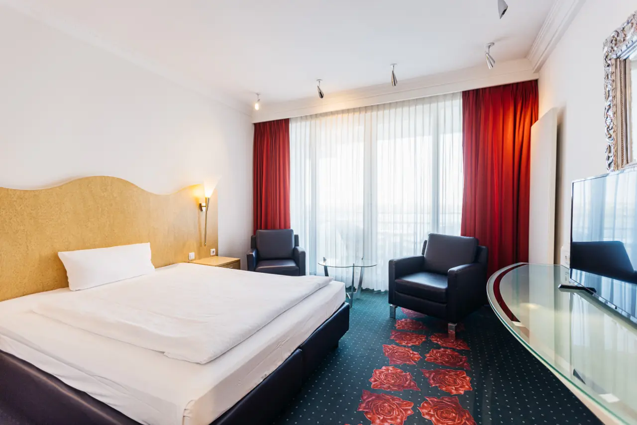 Helles Hotelzimmer im Vitalia Seehotel mit Doppelbett, Sitzgelegenheit und Balkonzugang.