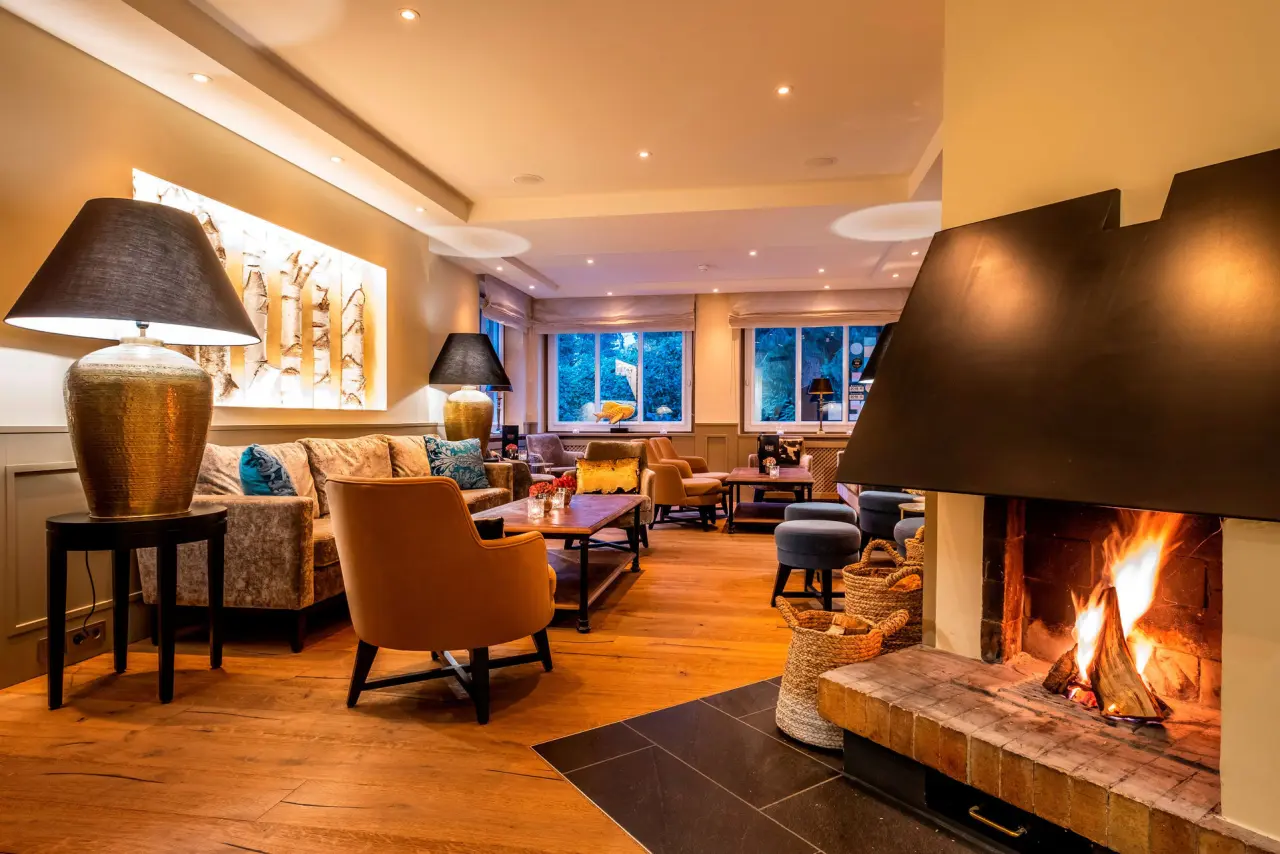 Gemütliche Hotellobby mit knisterndem Kamin und bequemen Sitzgelegenheiten im Hotel Birke, ideal zum Entspannen.