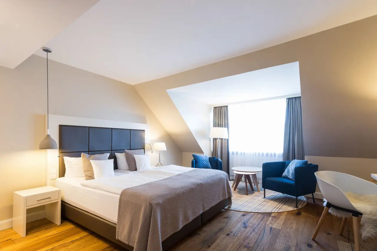Modernes Hotelzimmer mit gemütlichem Doppelbett, blauen Sesseln und Holzboden im Hotel Birke.