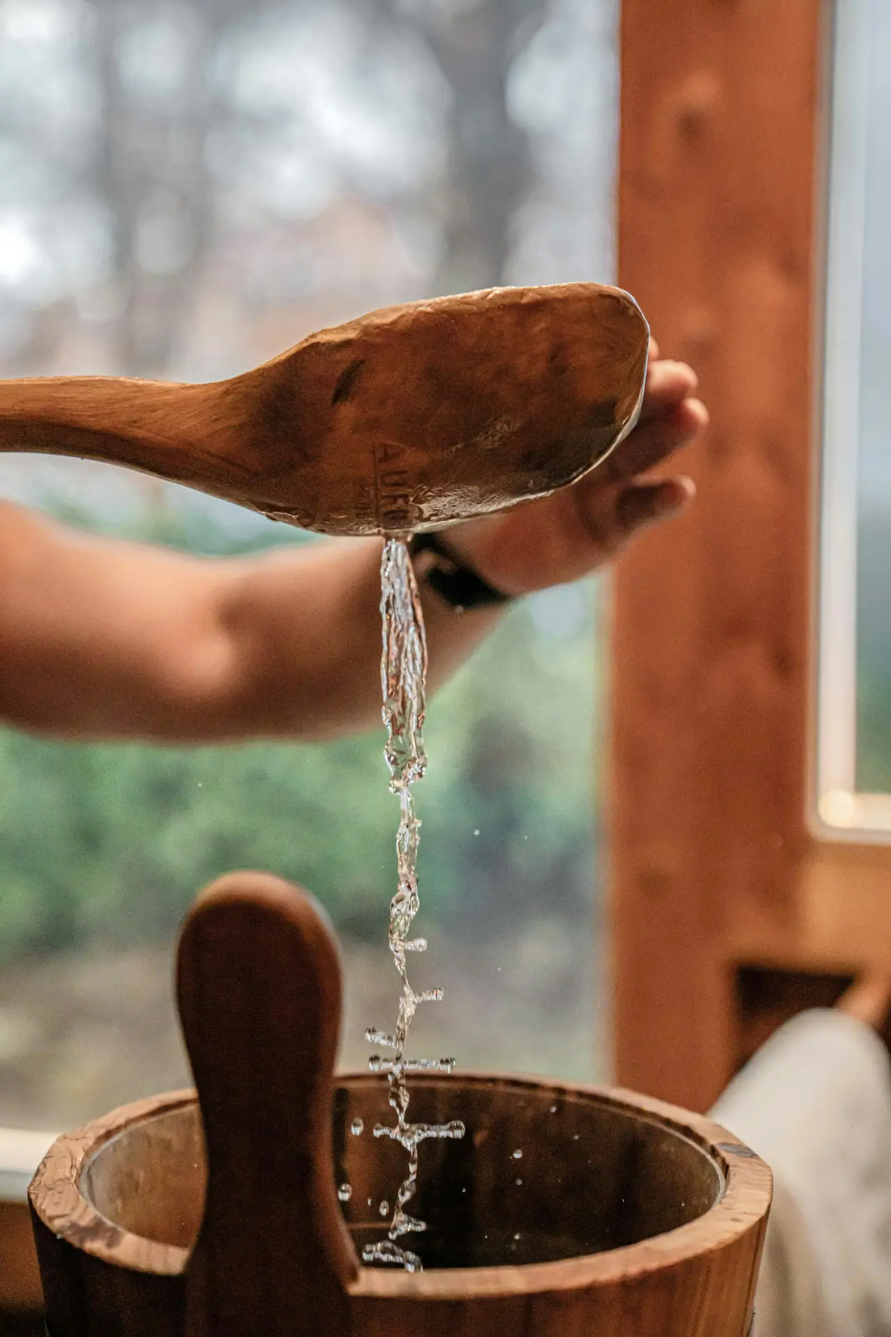 Aufguss in der Sauna des BEATUS Wellness- & Spa-Hotels: Wasser wird mit Holzkelle in Saunakübel gegossen.