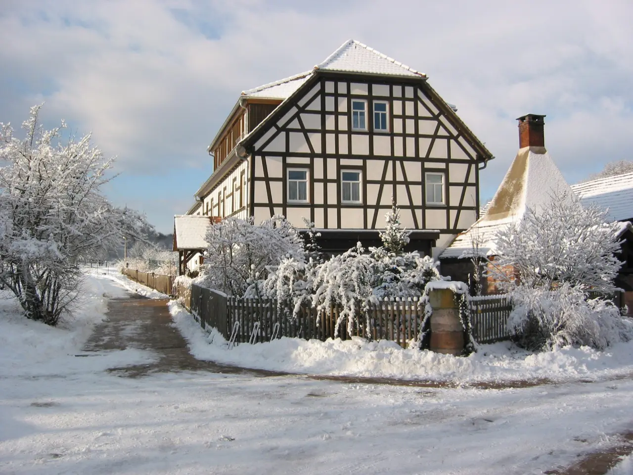 Historisches Fachwerkhaus des Hotel Hammermühle im Winter, umgeben von verschneiten Bäumen und Wegen unter blauem Himmel.