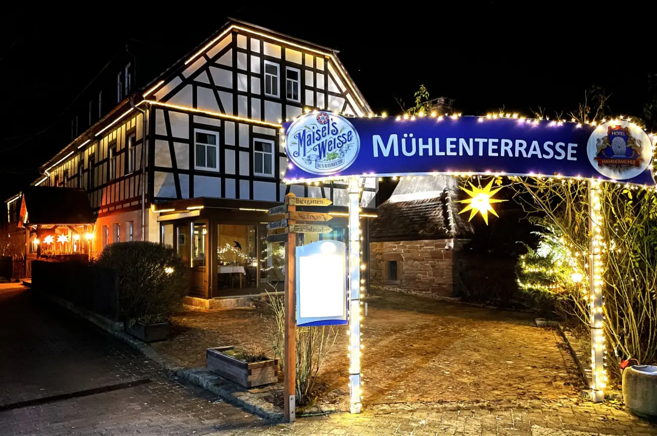 Festlich beleuchteter Eingangsbereich des Hotel Hammermühle bei Nacht mit Fachwerkhaus und Wegweisern.