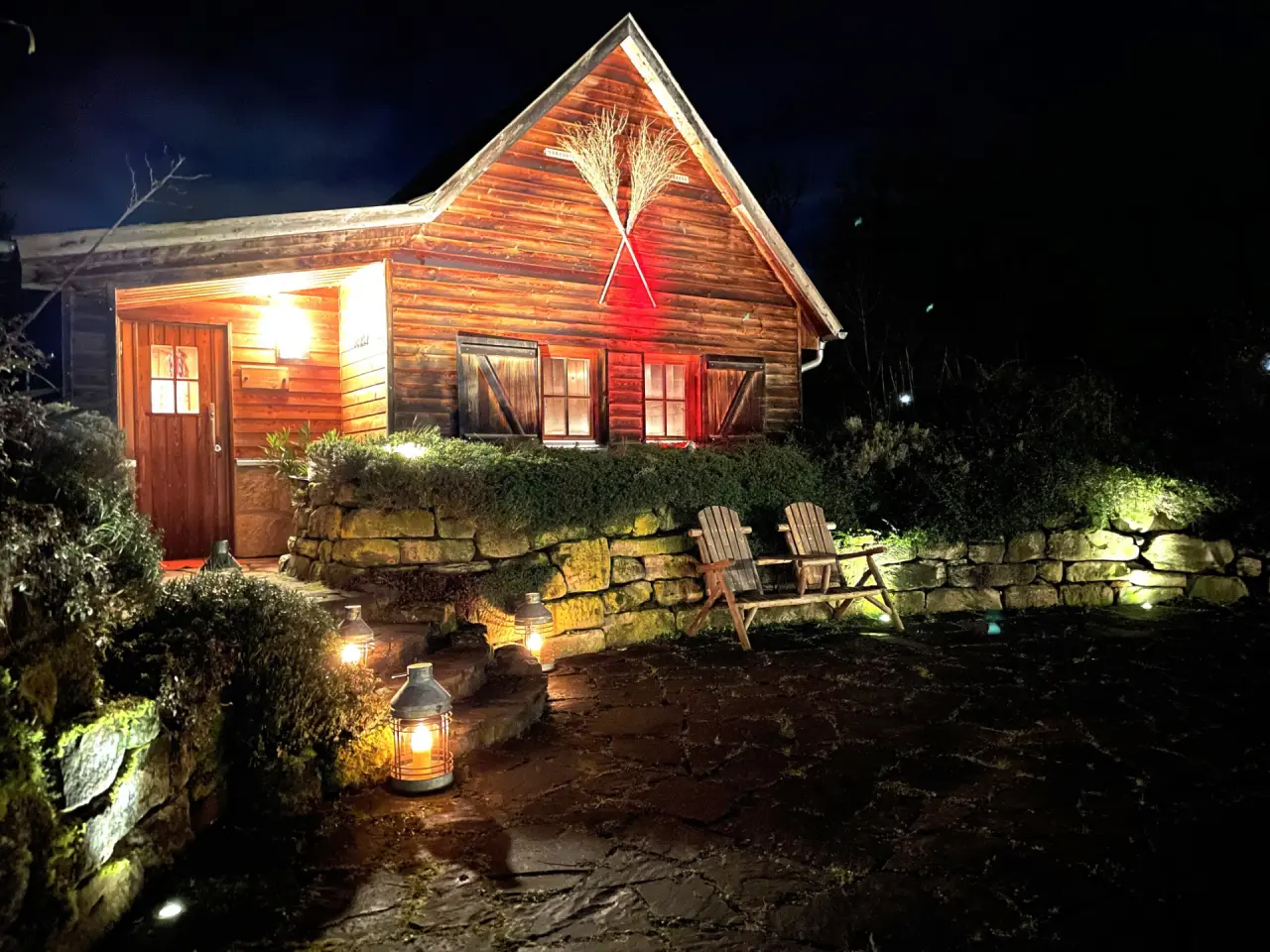 Beleuchtetes Holzhaus des Hotel Hammermühle bei Nacht mit Laternen und rustikalen Holzstühlen im Gartenbereich.