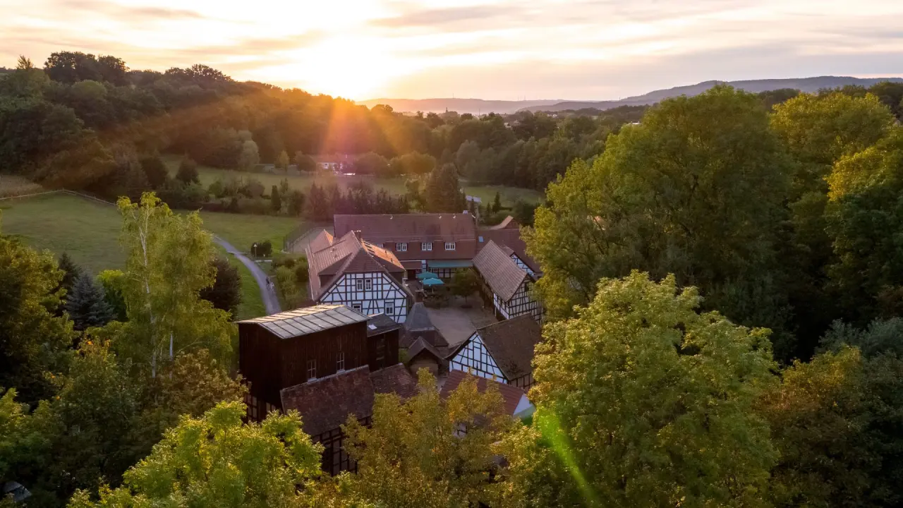 Luftaufnahme des Hotel Hammermühle im Sonnenuntergang, umgeben von grünen Wäldern und Feldern. Idyllische Fachwerkhäuser.