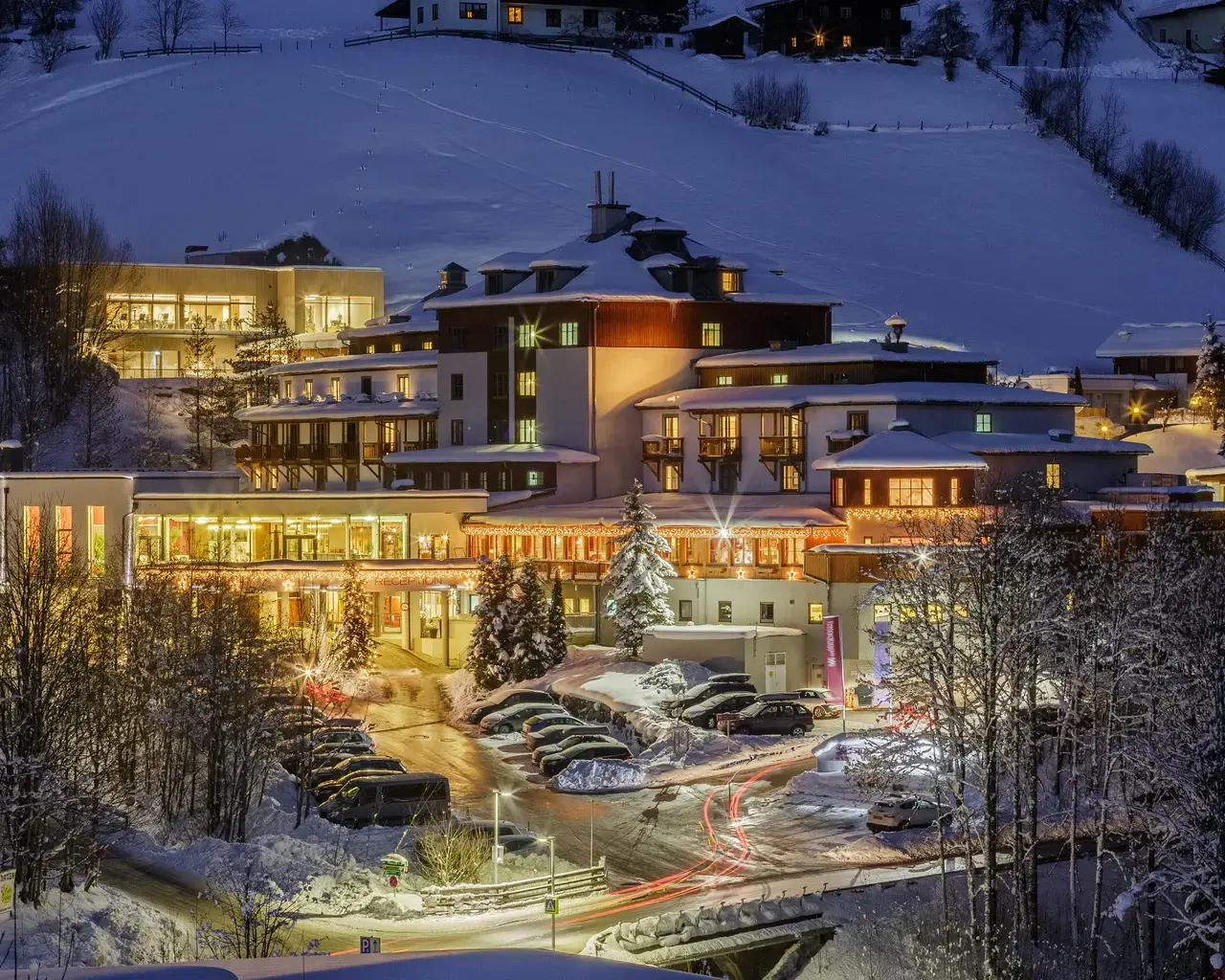 Sporthotel Wagrain im Winter bei Nacht. Das beleuchtete Hotelgebäude liegt eingebettet in eine verschneite Berglandschaft.