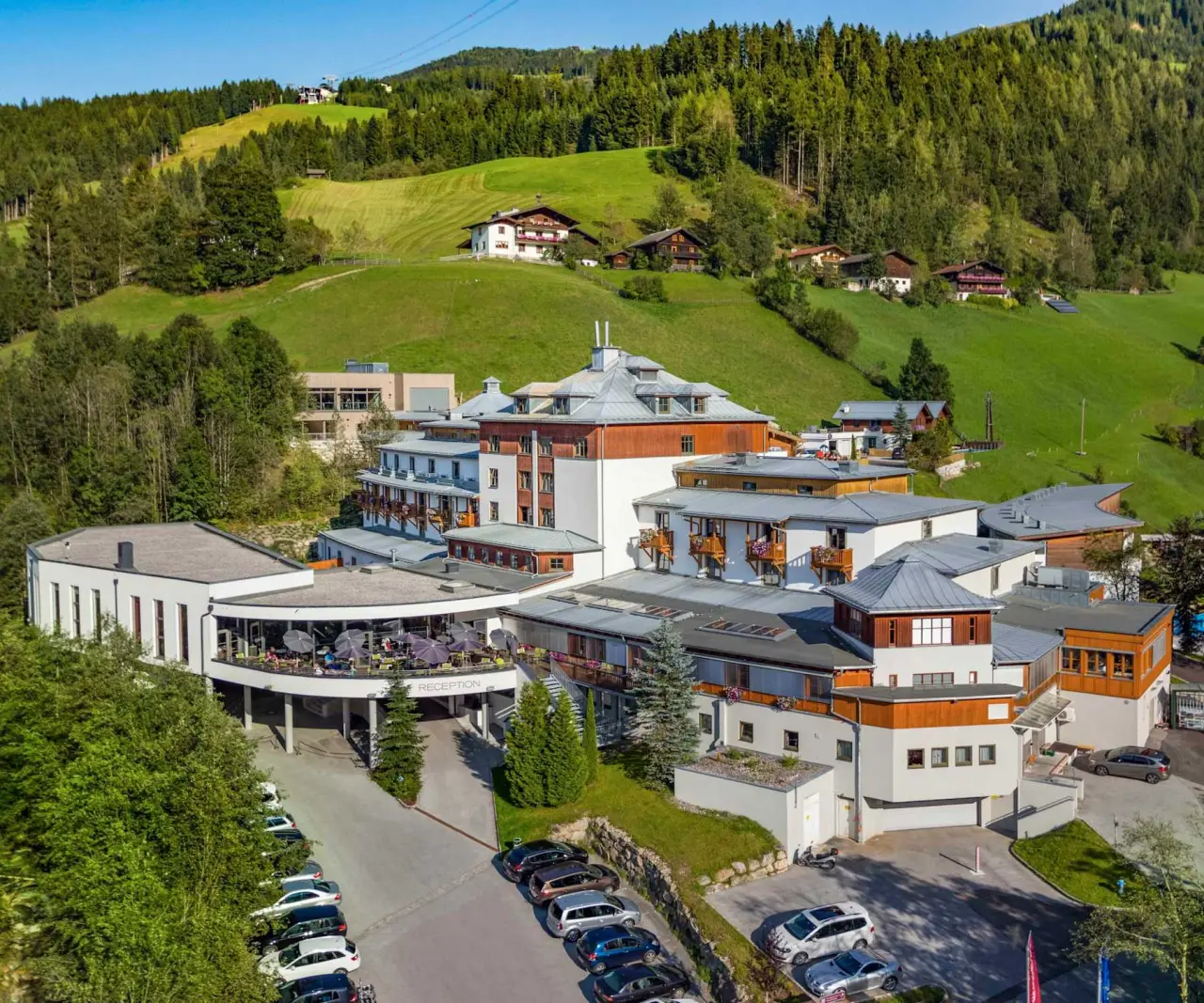 Luftaufnahme des Sporthotel Wagrain in den österreichischen Alpen, umgeben von grünen Hügeln und Wäldern.