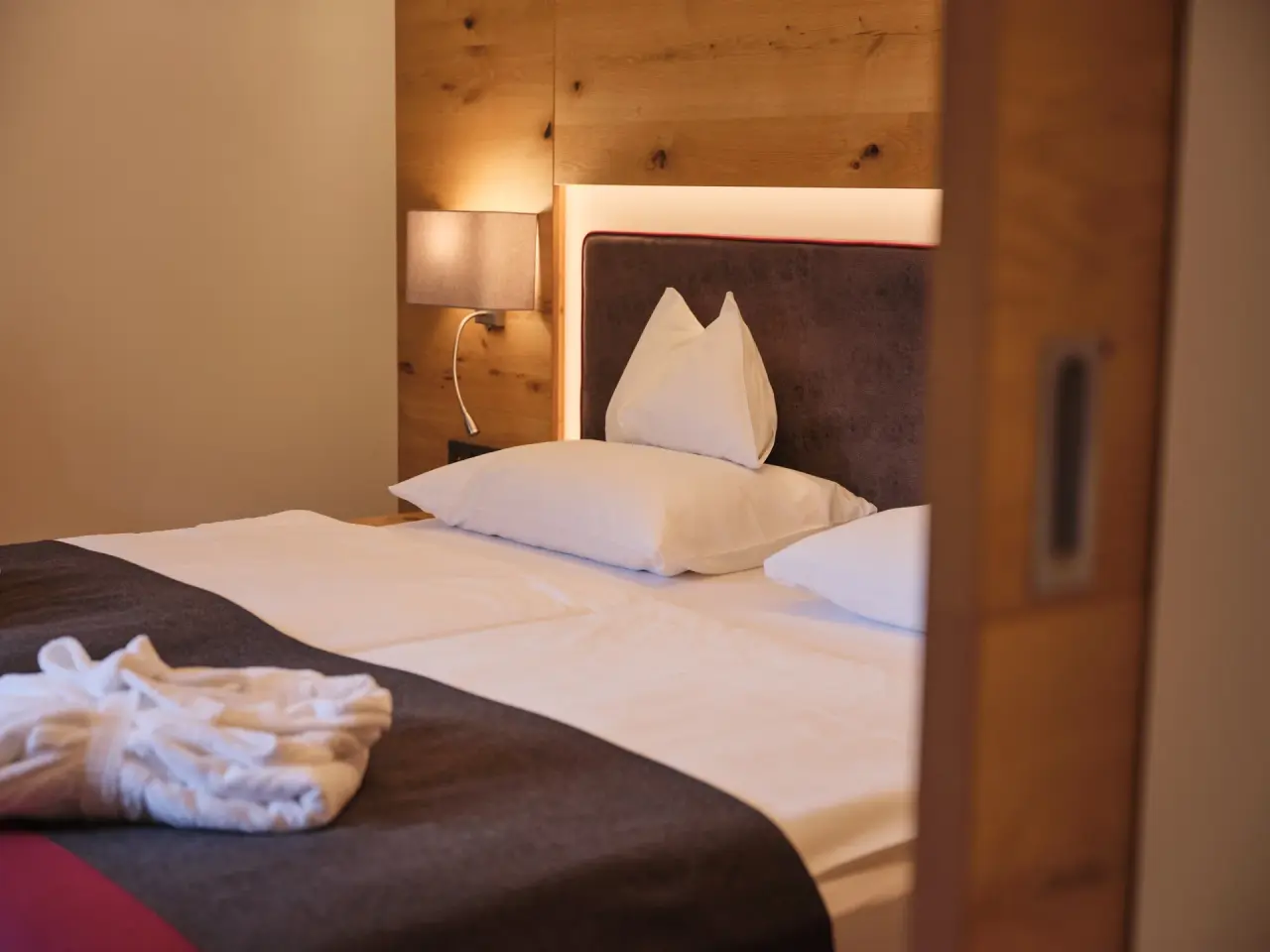 Gemütliches Doppelzimmer mit Holzwand, Leselampe und Bademantel im Sporthotel Wagrain