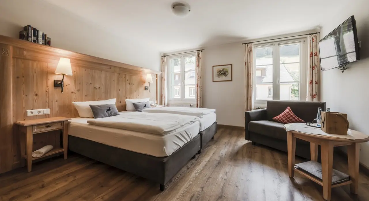 Gemütliches Doppelzimmer im Naturparkhotel Grüner Baum mit Holzvertäfelung, bequemen Betten und Sitzbereich.