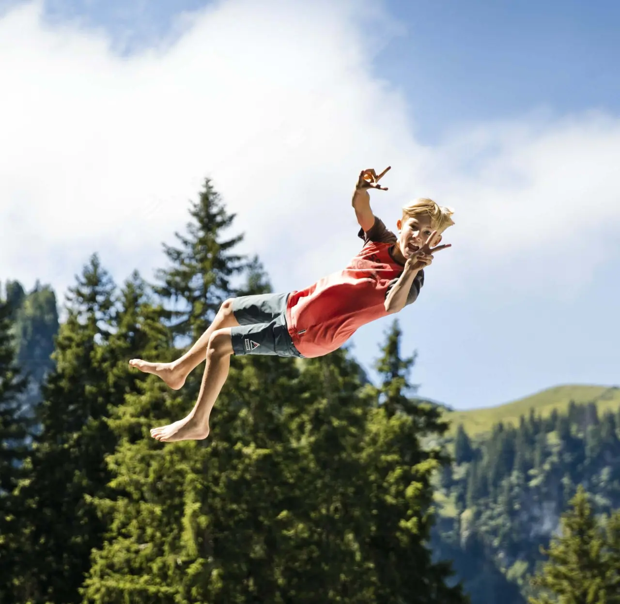 Fröhlicher Junge springt in die Luft vor Bergpanorama, steht für aktive Familienferien im Wellness- & Familienhotel Egger.