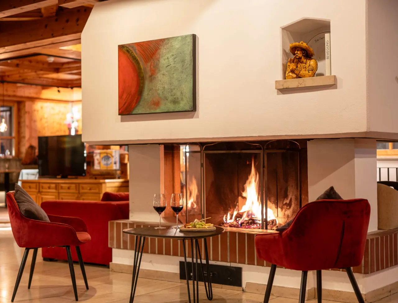Gemütliche Hotellounge mit knisterndem Kamin, roten Sesseln, Wein und Snacks im Wellness- & Familienhotel Egger.