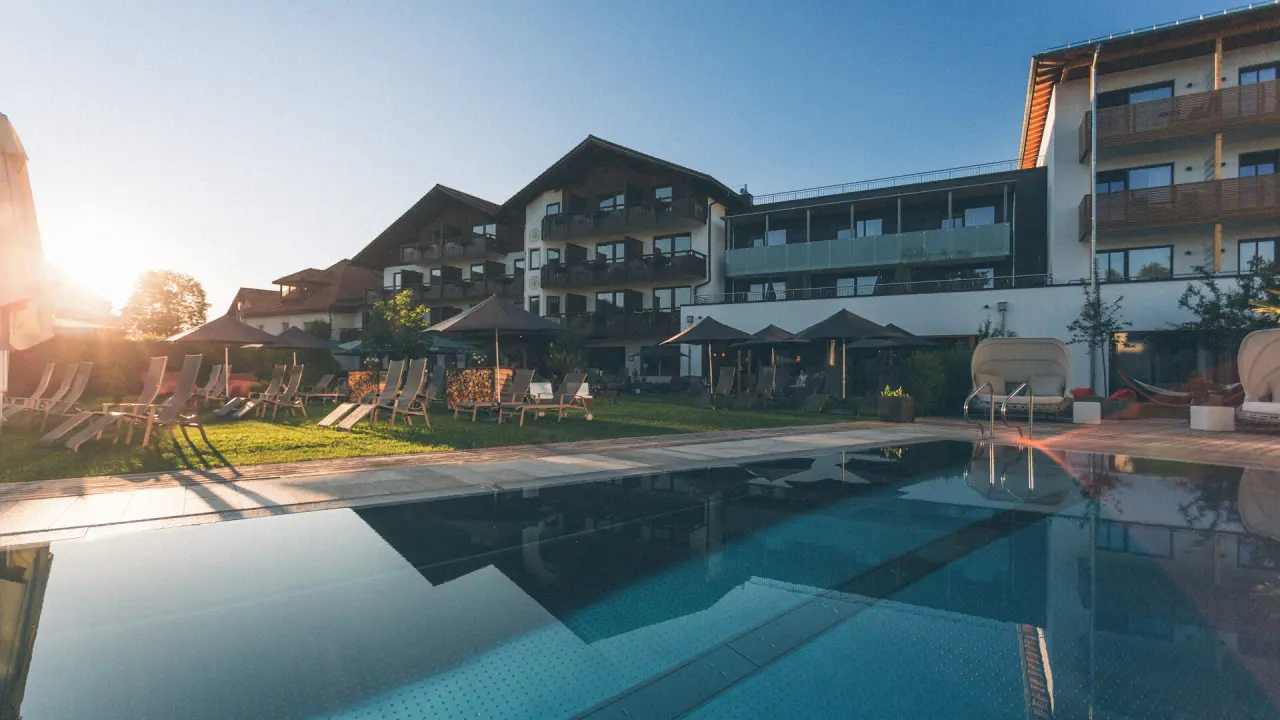 Aussenpool des Hotel Eibl-Brunner bei Sonnenuntergang mit Liegewiese und Hotelgebäude im Hintergrund. Entspannung pur.