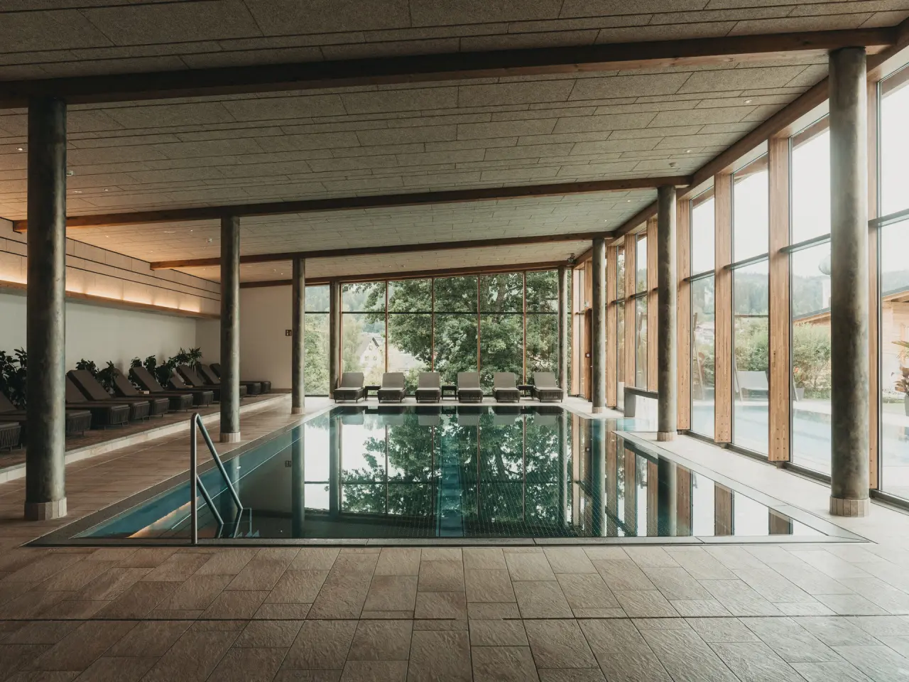 Heller Innenpool im Hotel Eibl-Brunner mit großen Panoramafenstern und Blick ins Grüne, umgeben von bequemen Liegen.
