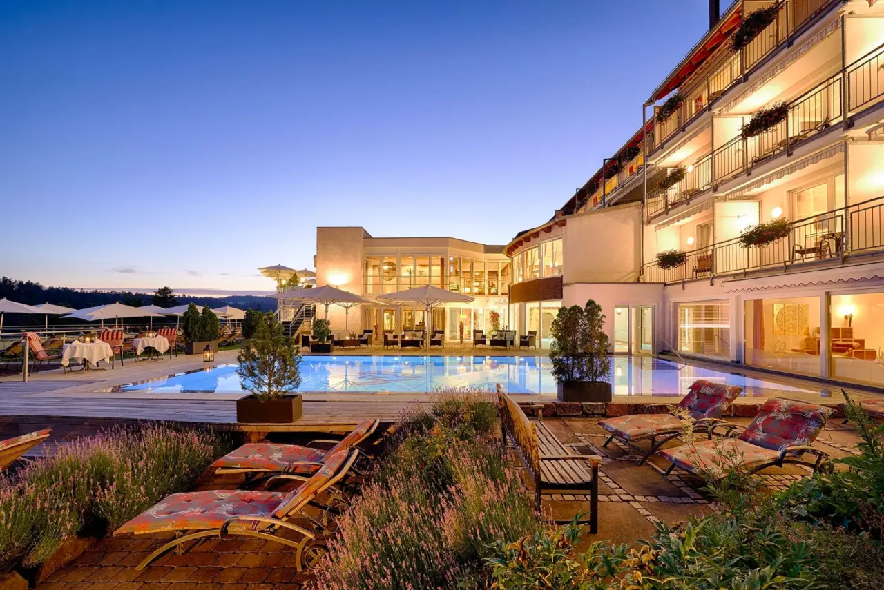 Beleuchteter Aussenpool mit Liegestühlen und Hotelgebäude bei Dämmerung im Berlins KroneLamm.