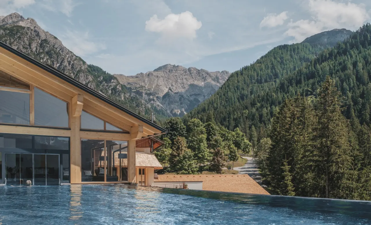 Almwellness-Resort Tuffbad: Infinity Pool mit atemberaubendem Bergpanorama und moderner Holzarchitektur.