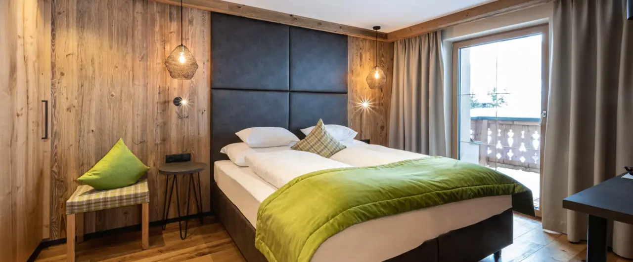 Gemütliches Doppelzimmer im Alpenresort Fluchthorn mit Holzelementen, Balkon und Blick auf die Winterlandschaft.
