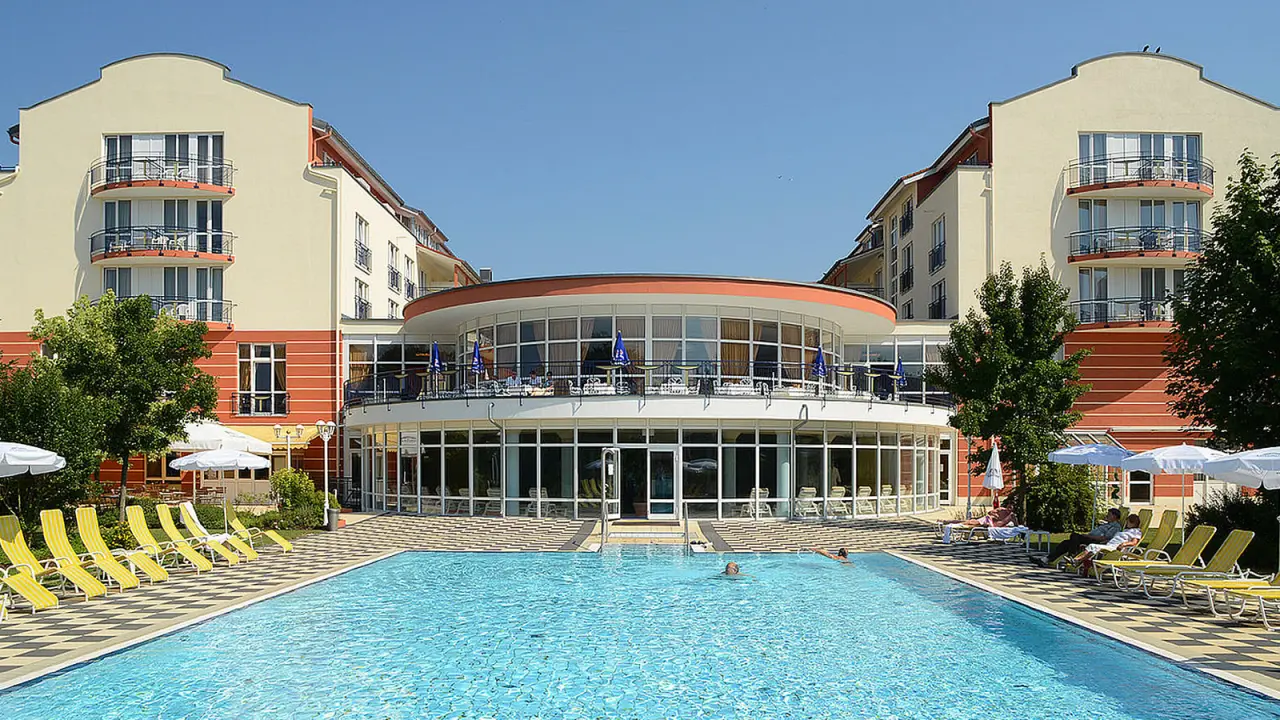 Großer Außenpool mit Liegestühlen und Hotelgebäude unter blauem Himmel im The Monarch Hotel.