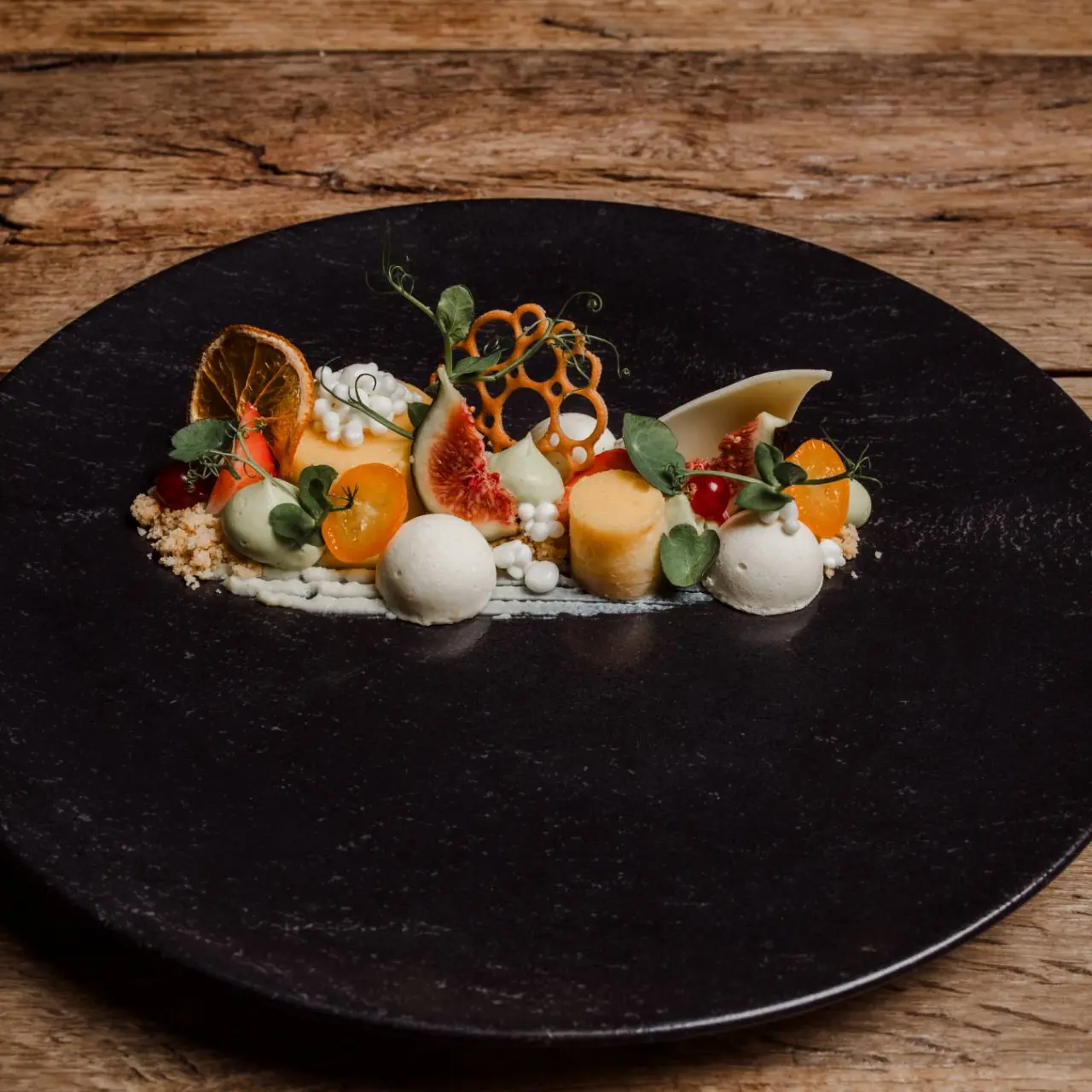 Exquisit angerichtetes Dessert mit frischen Früchten und Eis auf einem schwarzen Teller im Restaurant des Hotel Kaiserhof.