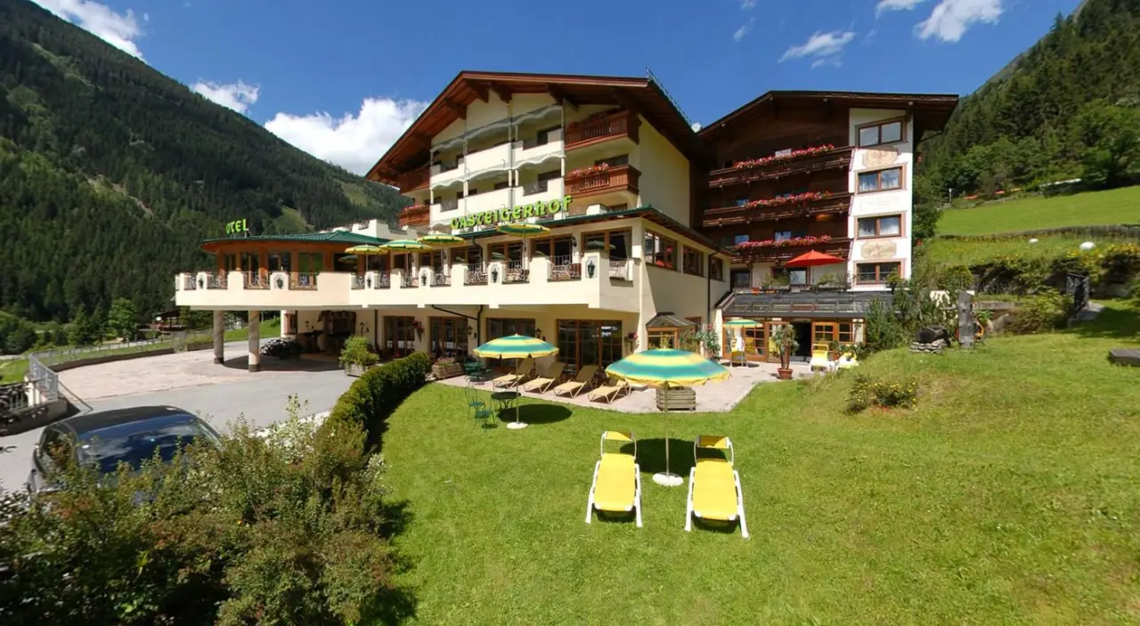 Alpenwellness Hotel Gasteigerhof in den Tiroler Alpen. Traditionelles Hotelgebäude mit Balkonen, sonnigem Garten und Liegewiese.