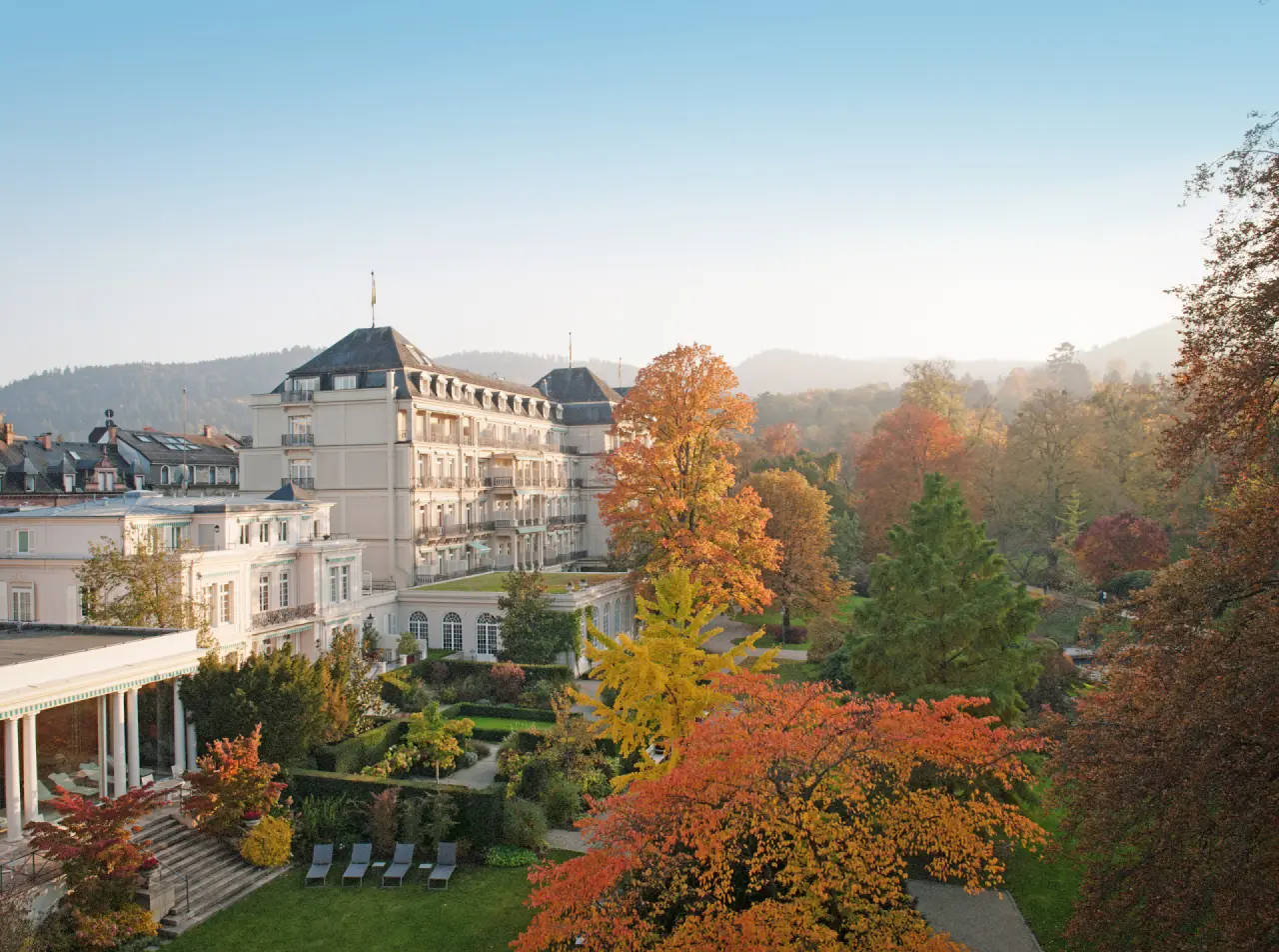 Majestätisches Brenners Park-Hotel & Spa mit weitläufigem Park in herbstlicher Farbenpracht und sanften Hügeln im Hintergrund.