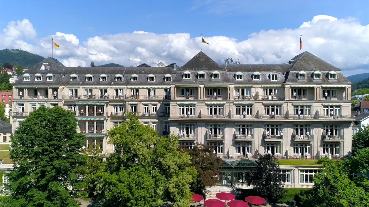 Majestätische Aussenansicht des Brenners Park-Hotel & Spa in Baden-Baden mit grünen Bäumen und blauem Himmel.