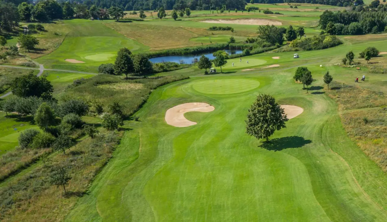 Luftaufnahme des weitläufigen Golfplatzes mit Wasserhindernis und Spielern im Balmer See - Hotel·Golf·Spa.
