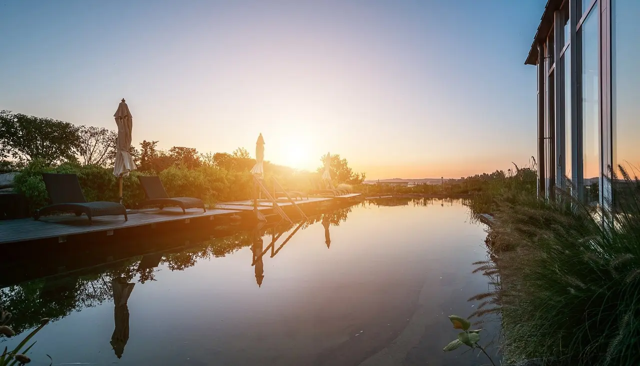 Naturschwimmteich des Balmer See - HotelGolfSpa bei Sonnenuntergang mit Liegen und Hotelgebäude.