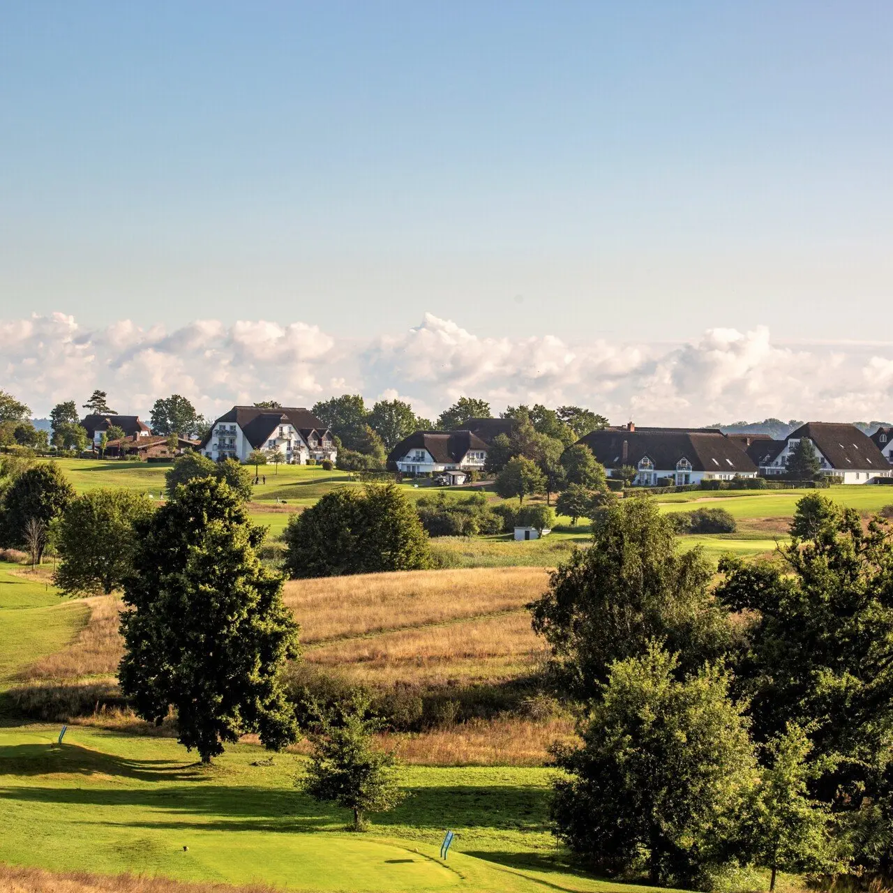 Weitläufiger Golfplatz und charmante Hotelgebäude des Balmer See - Hotel·Golf·Spa auf Usedom unter blauem Himmel.