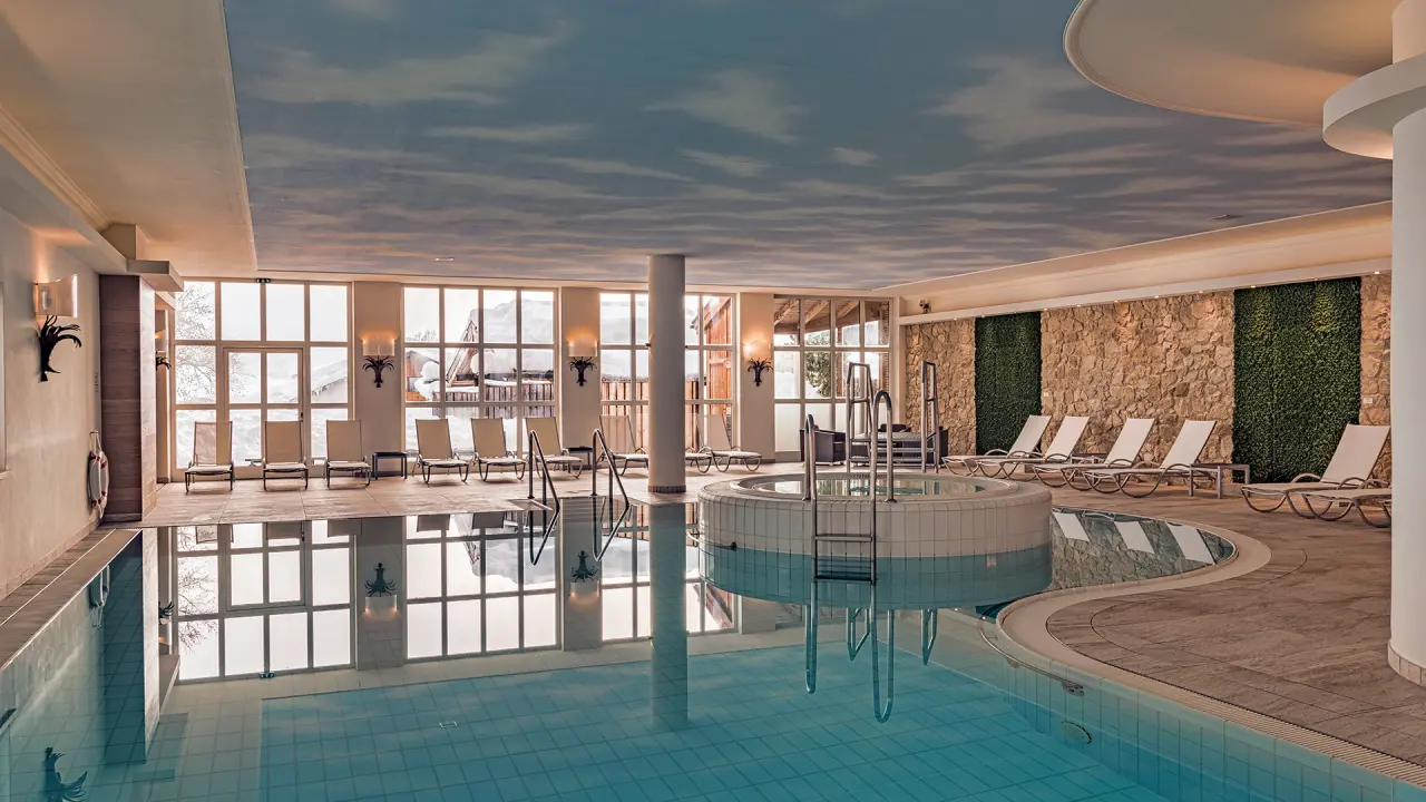 Grosszügiger Innenpool mit Whirlpool und Liegebereich im Hotel Unterwirt. Blick auf die verschneite Winterlandschaft.