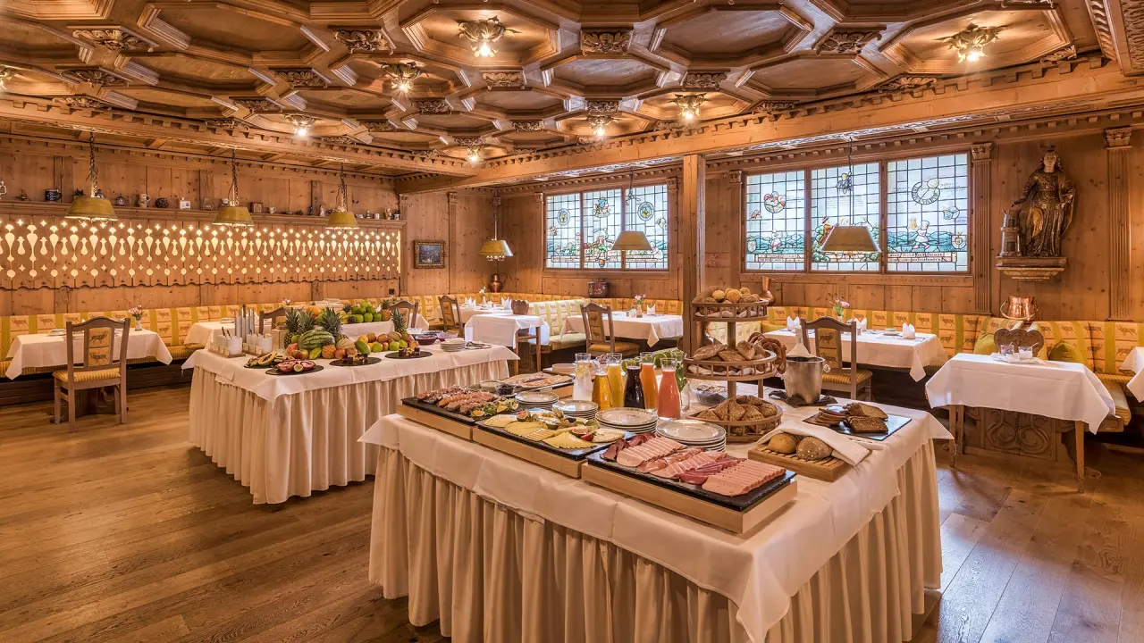 Reichhaltiges Frühstücksbuffet im traditionellen Restaurant des Hotel Unterwirt mit holzgetäfelten Wänden und Buntglasfenstern.