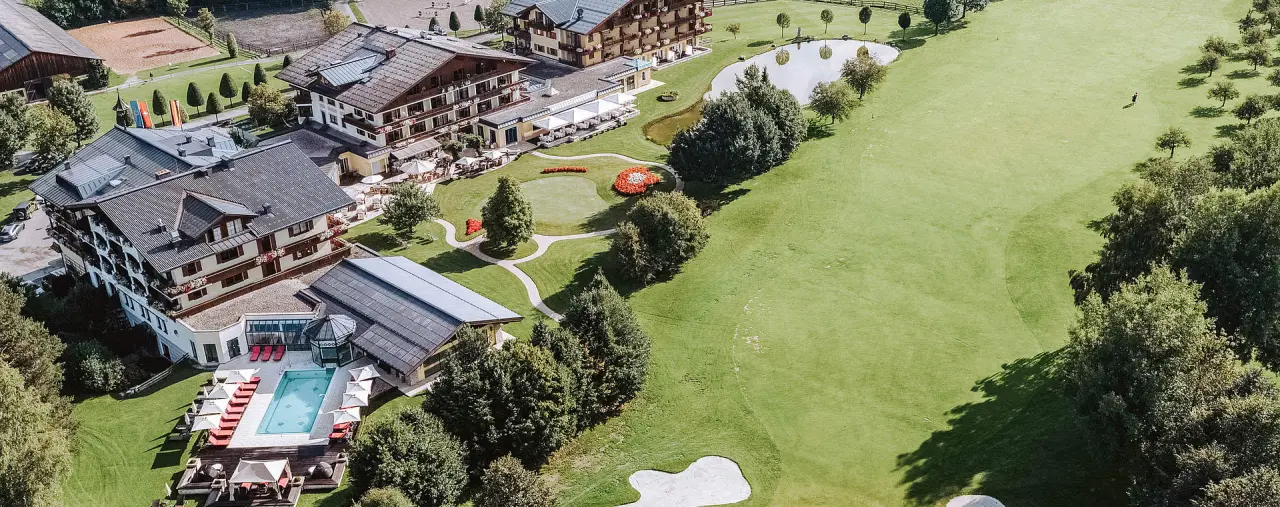 Luftaufnahme vom Hotel Gut Weissenhof Radstadt: Hotelanlage mit Aussenpool, Golfplatz und weitläufiger grüner Landschaft.