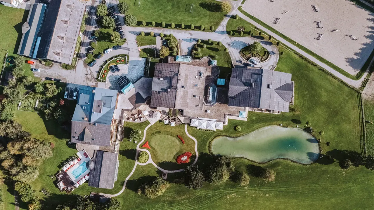 Luftaufnahme des Hotel Gut Weissenhof Radstadt mit weitläufiger Anlage, Aussenpool, Teich, Golf-Putting-Green und Reitplatz.