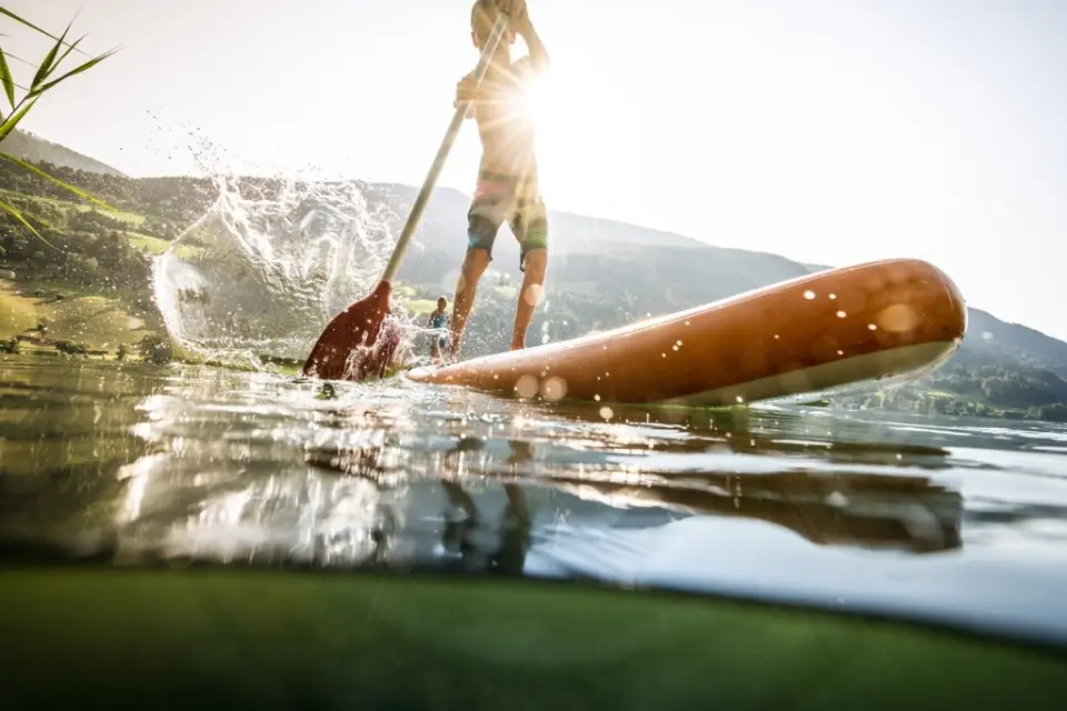 Kind beim Stand-Up-Paddling auf einem See mit Bergpanorama, Aktivität nahe DAS RONACHER Therme & Spa Resort.