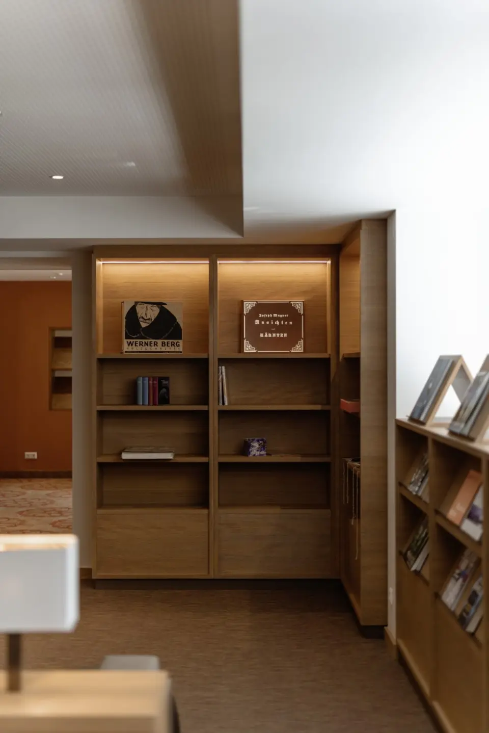 Modernes Bücherregal mit indirekter Beleuchtung in der gemütlichen Lounge des DAS RONACHER Therme & Spa Resort.