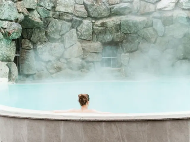 Gast entspannt im dampfenden Thermalpool mit Felswand im DAS RONACHER Therme & Spa Resort.