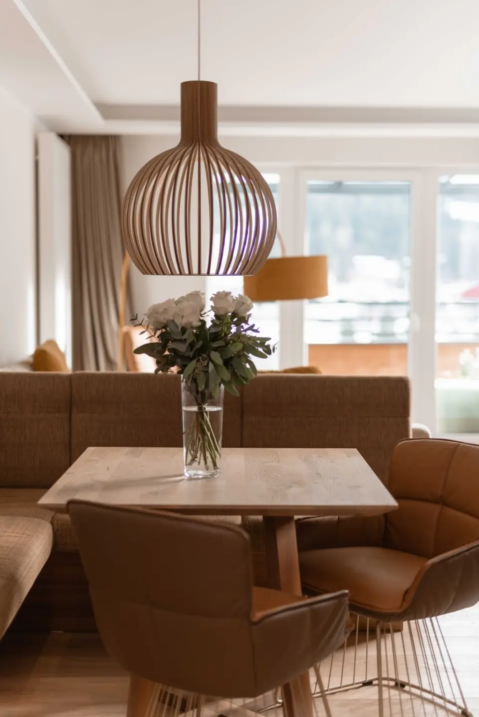 Moderner Wohnbereich in einer Suite des DAS RONACHER Therme & Spa Resort mit Holztisch, Design-Lampe und frischen Blumen.