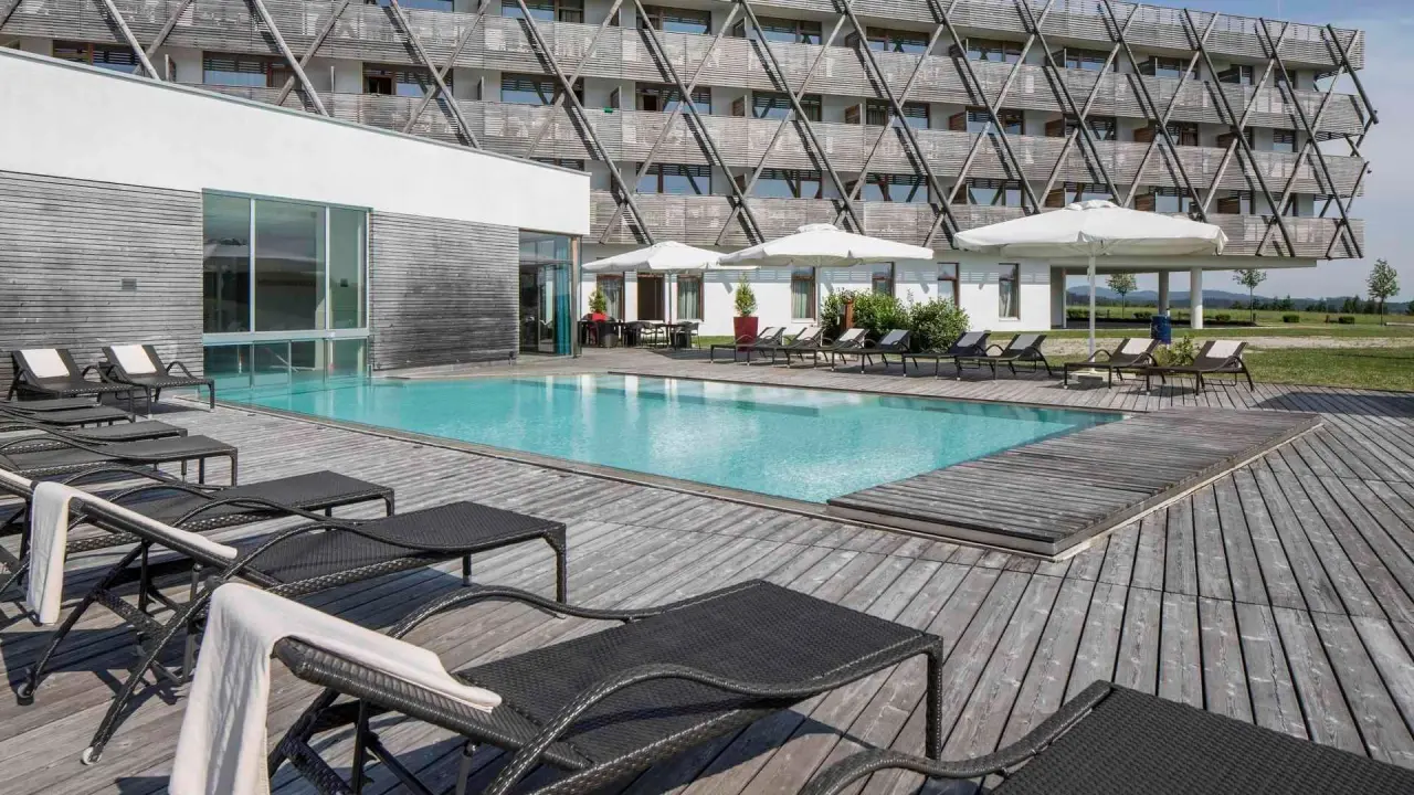 Aussenpool mit Holzterrasse und Liegen vor der modernen Hotelfassade des Falkensteiner Genuss & Wohlfühlhotel Mühlviertel.