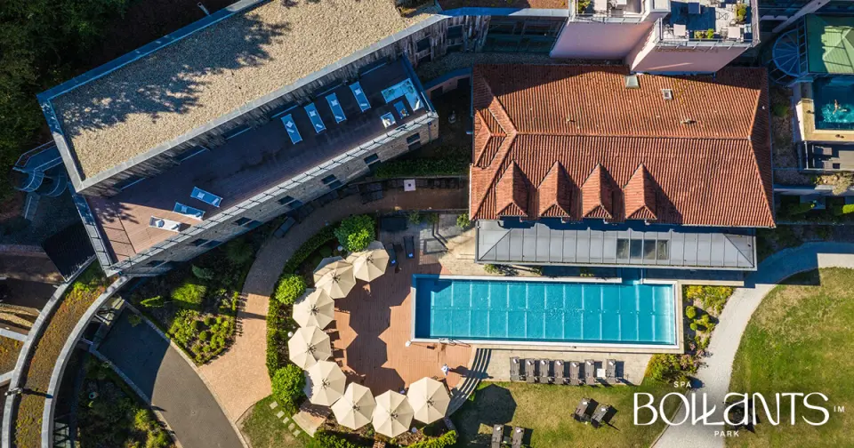 Luftaufnahme des BollAnts Spa im Park mit Aussenpool, Sonnenterrasse und Hotelgebäuden in grüner Umgebung.