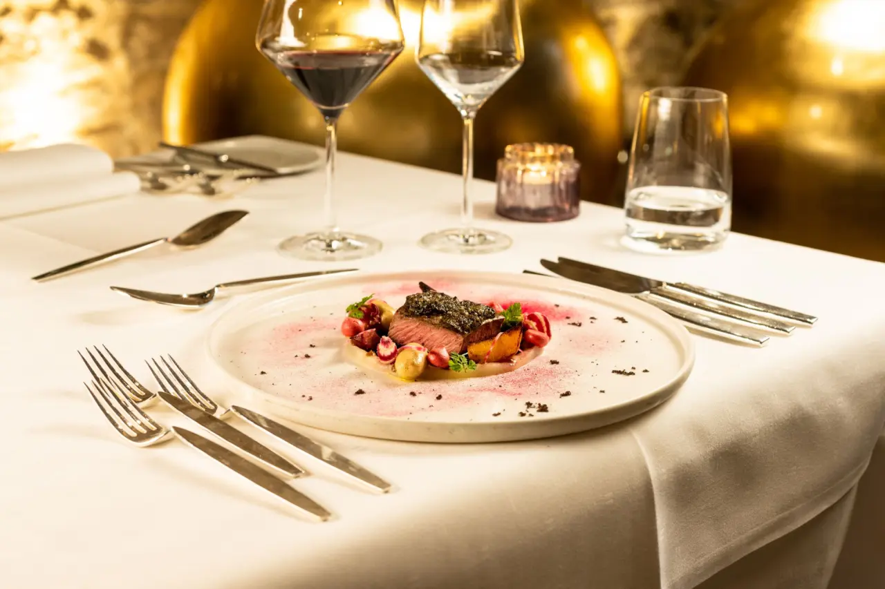 Exquisit angerichtetes Gericht im Gourmetrestaurant des BollAnts Spa im Park, mit Rotwein und Kerzenlicht.