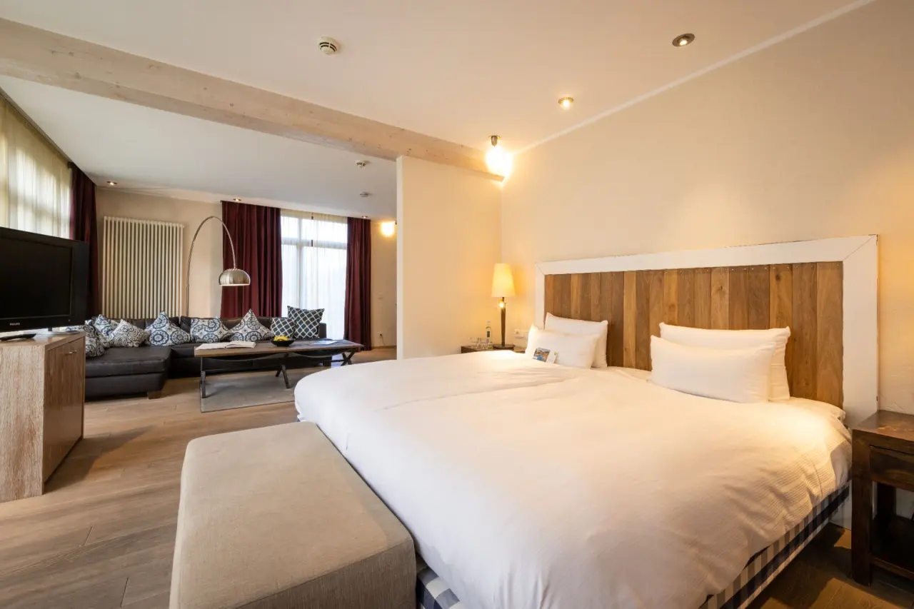 Geräumiges Hotelzimmer mit Doppelbett und separatem Wohnbereich im BollAnts Spa im Park. Gemütliche Einrichtung mit Holzelementen.