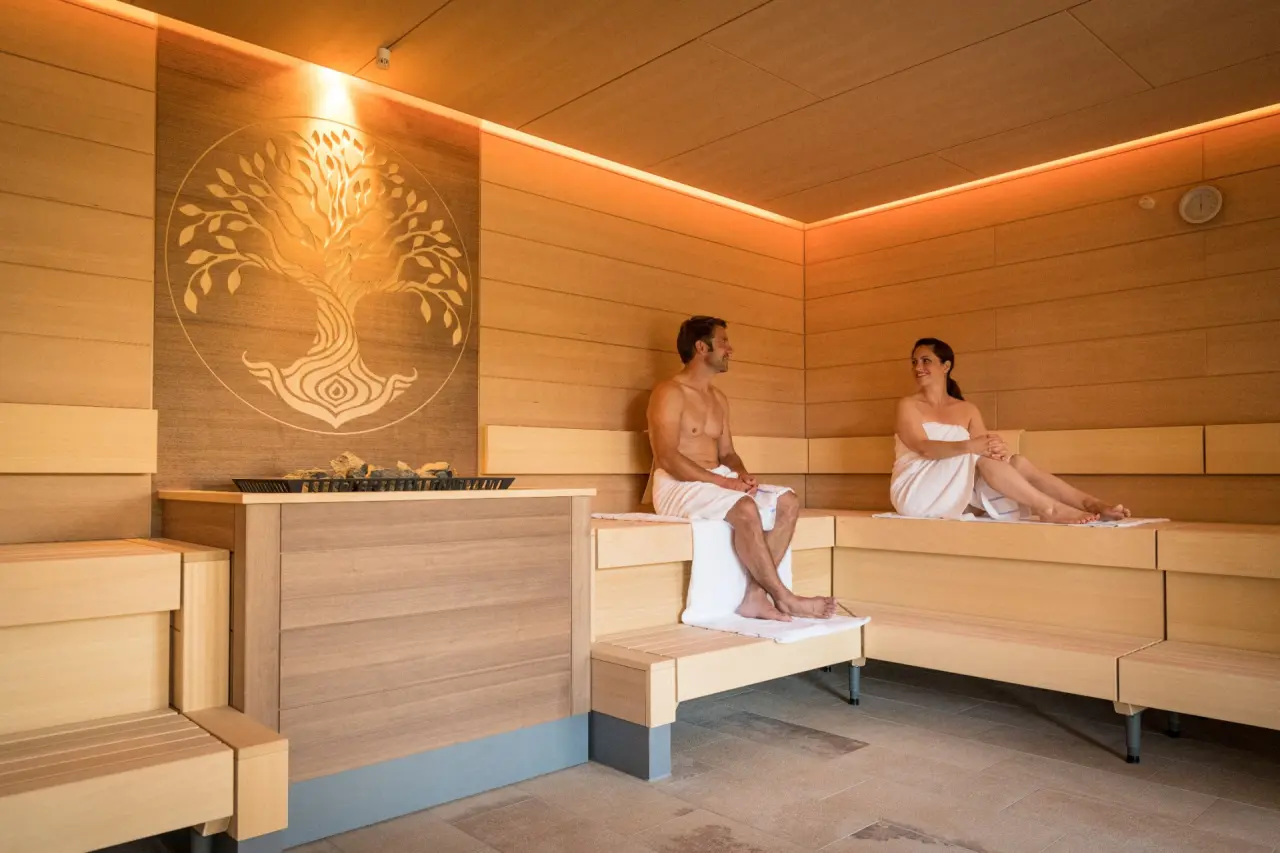 Modern gestaltete Sauna mit 'Baum des Lebens'-Wandkunst und entspannendem Paar im BollAnts Spa im Park.
